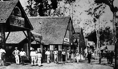 A group of residents of 1860s Gympie posing for a photo on the main street of town in front of shingle roofed buildings