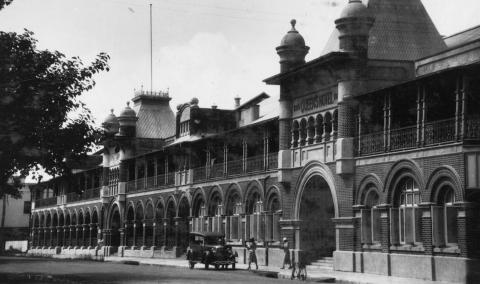 View of Queens Hotel, Townsville, featuring cars and patrons. 