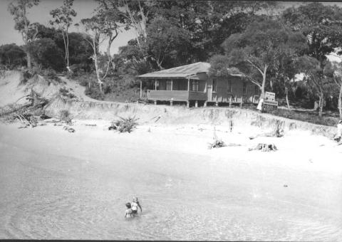 Black and white photograph of wooden cottage beside the beach at Amity Point. 