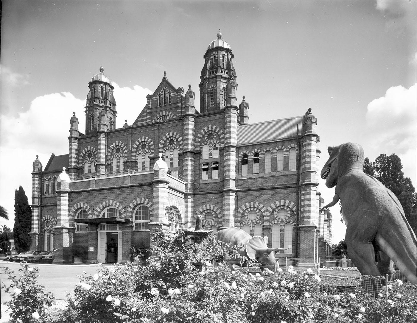 Front view of the old Queensland Museum with T. rex and triceratops dinosaur statue to the right