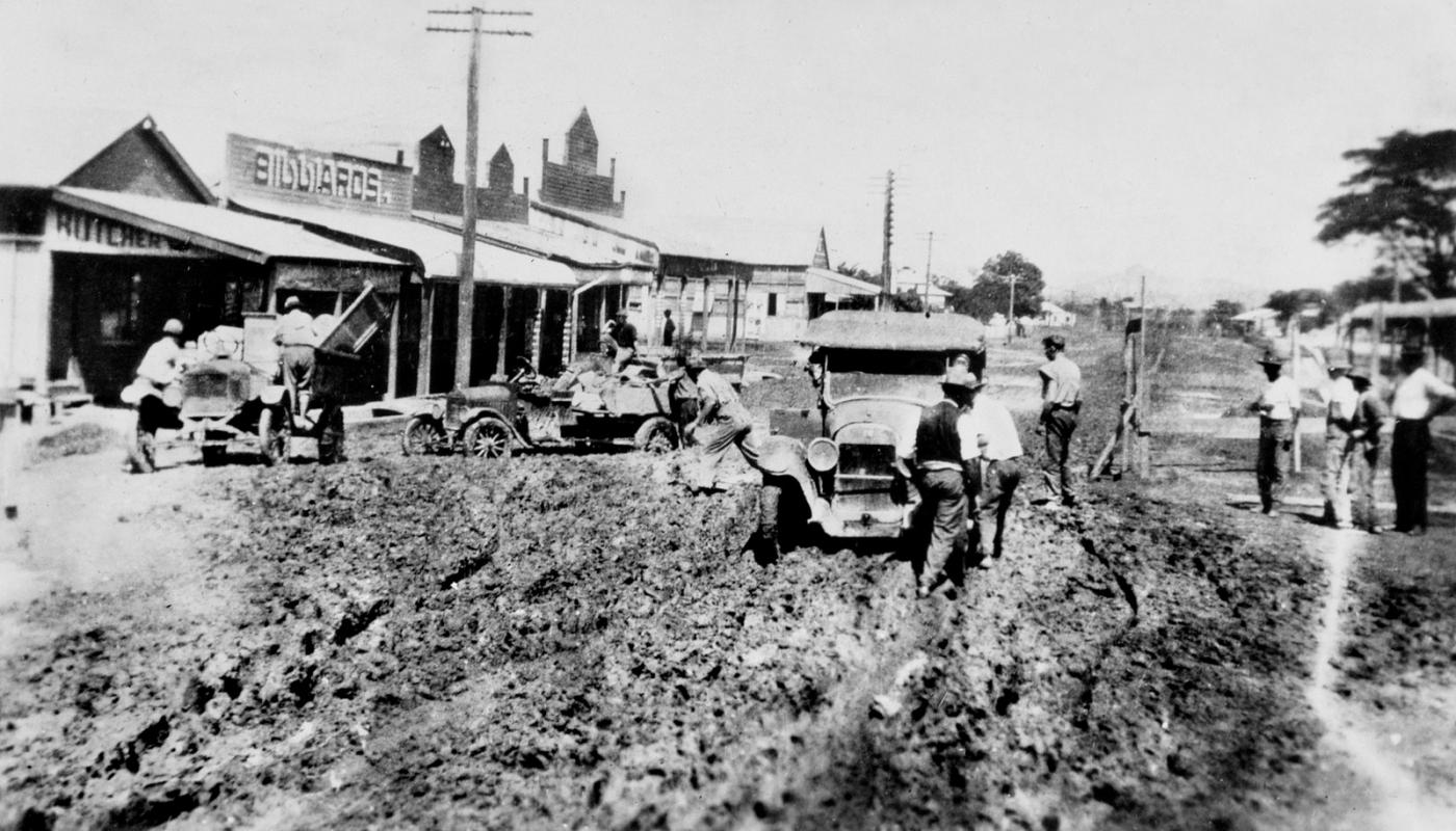 View of a dirt street congested with cars struggling to pass through the deep muddy holes