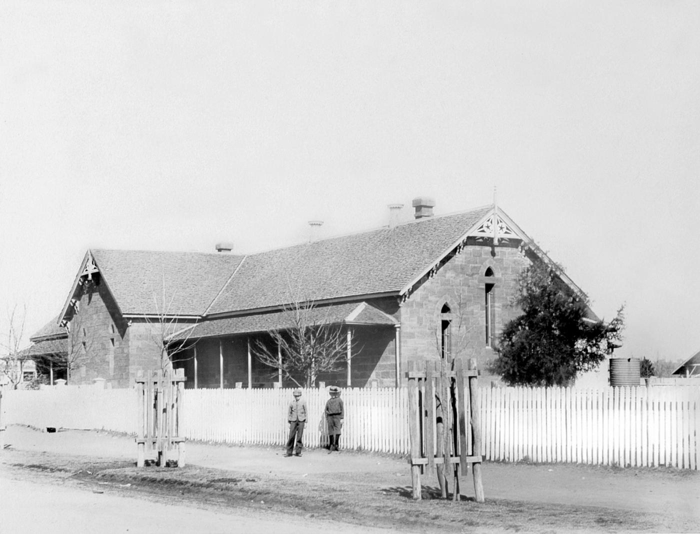 Exterior of Warwick public school, a single building with a few people gathered out the front