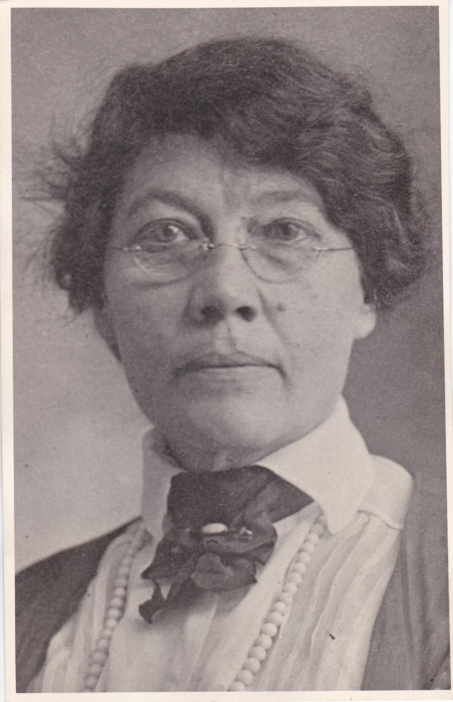 Black and white photograph of Mary Elizabeth Campbell, probably taken around 1919.  She is wearing small half-glasses, and a dark dress over white blouse with a ribbon rosette at the throat.  She also appears to be wearing a string of pearls.