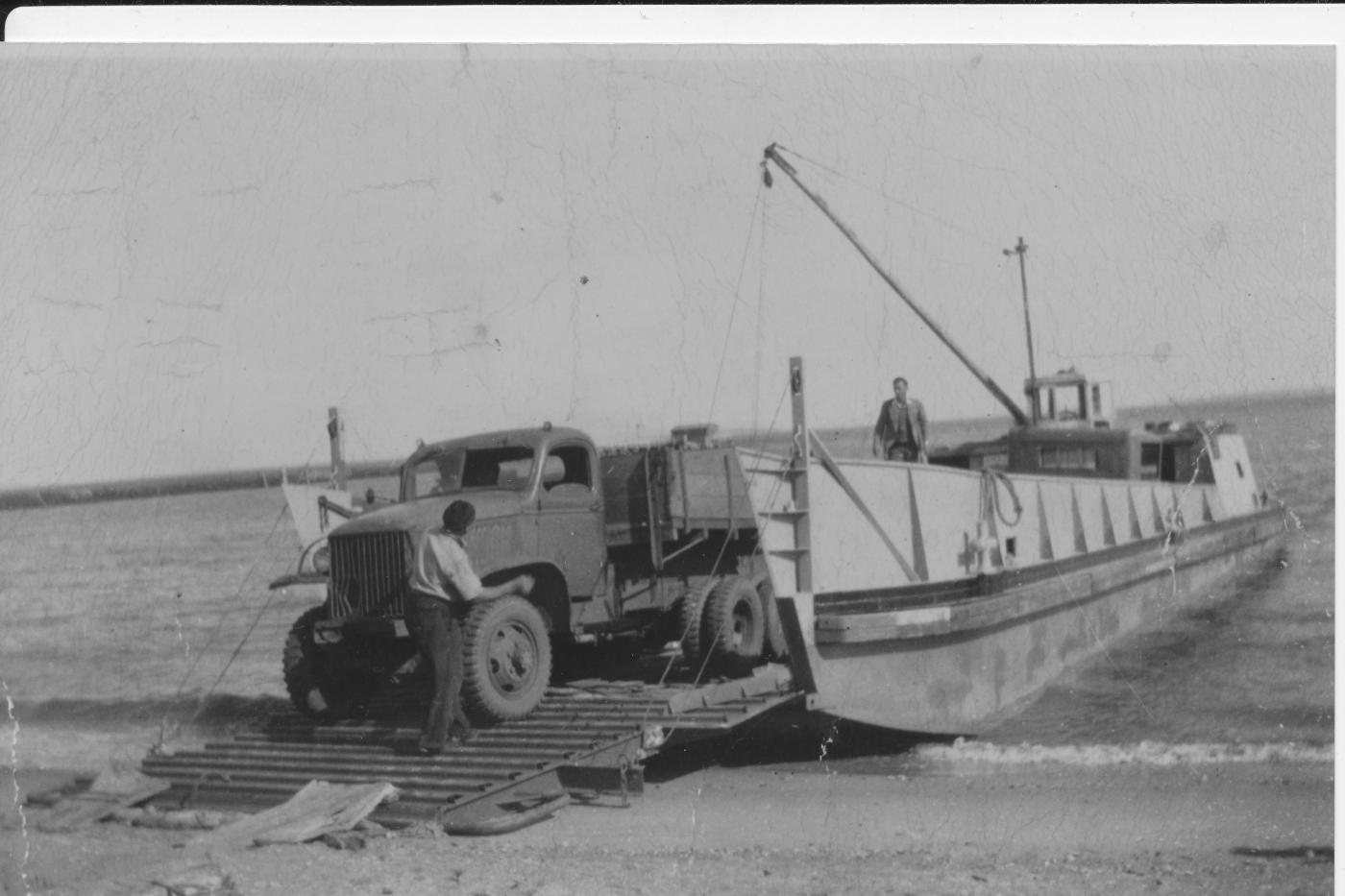 Sand trucks being unloaded from the barge onto the beach ca 1957