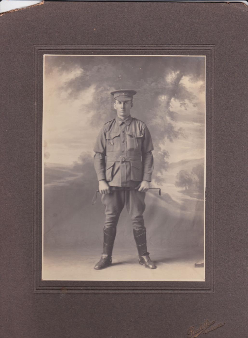 Black and white photograph of John Gordon Leslie (Gordon) Campbell in his Light Horse Uniform, taken in a studio.  He wears a cap instead of the slouch hat, military tunic, riding breeches, leather leggings and boots, and carries a riding crop.